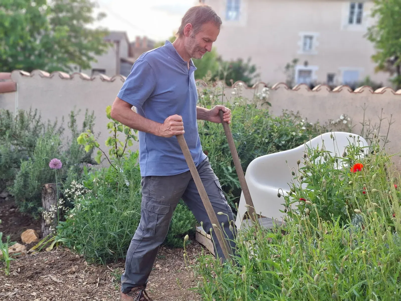 Christophe, Le Potagiste, travaille dans un jardin devant maison avec une bêche