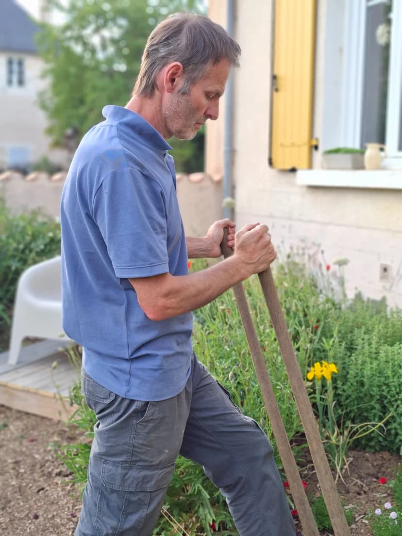 Christophe au travail de profil dans un jardin fleuri devant maison